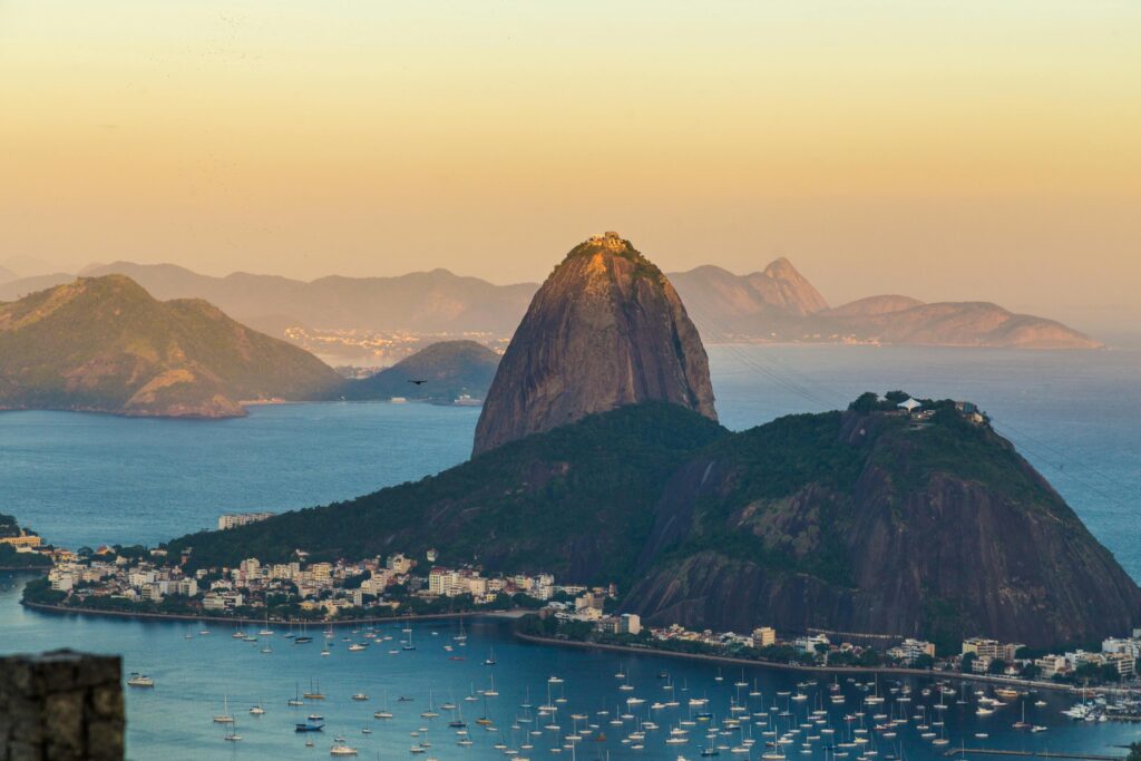 Imagem do Urca vista em dia de sol. Barcos no mar azul.